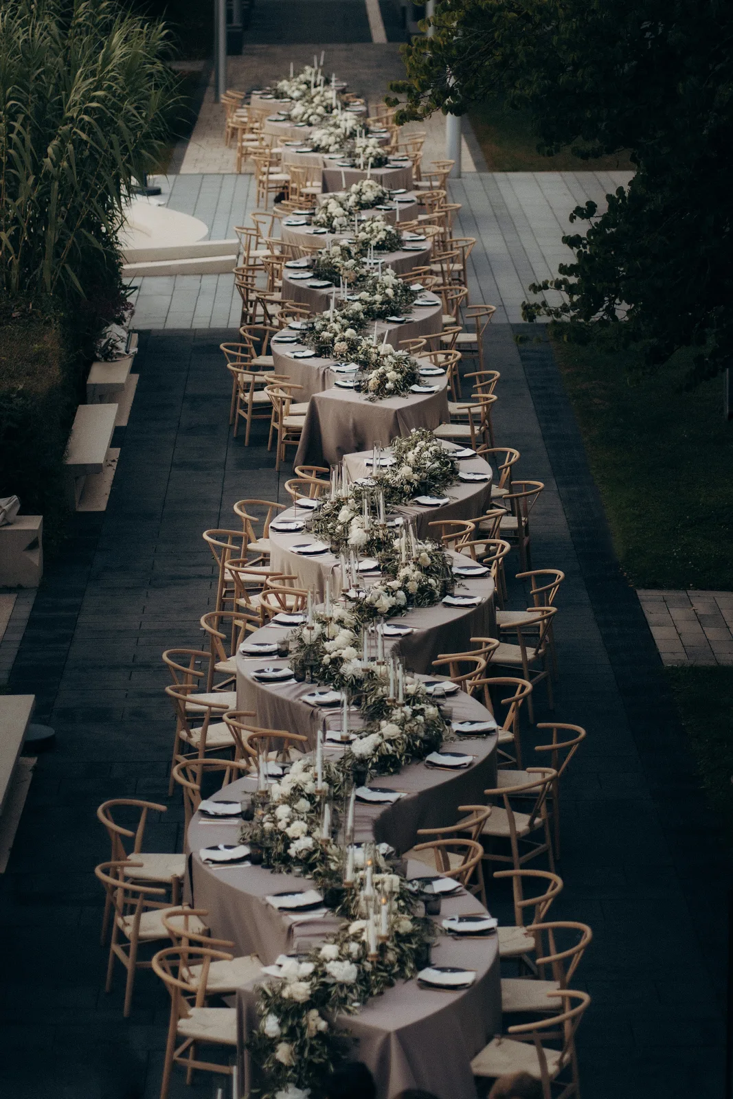 Geschwungene Hochzeitstafel mit weißer Floristik und Holzstühlen bei Nacht – Eventausstattung von vonRock Events