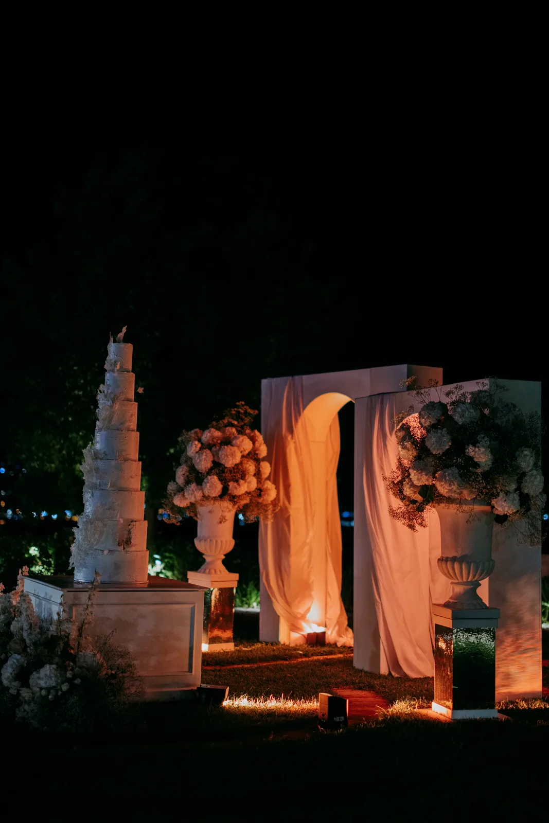 Mehrstöckige Hochzeitstorte vor beleuchteten Bögen mit Rosen bei Nacht